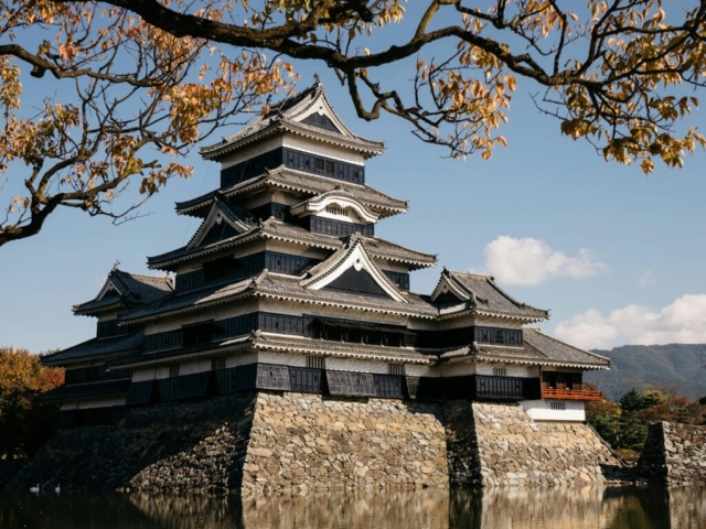 pexels-photo-29753529-29753529 Historic Matsumoto Castle surrounded by autumn foliage under a clear blue sky.