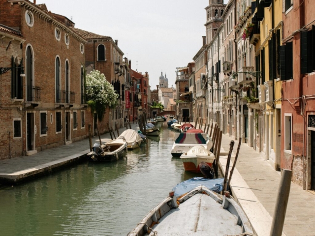 pexels-photo-5216366-5216366 A picturesque Venetian canal scene with colorful buildings and boats under a clear sky.