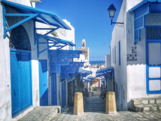 pexels-photo-891126-891126 Narrow cobblestone street with iconic blue and white architecture in Sousse, Tunisia, under a clear blue sky.